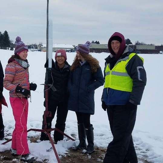 Moog mentor and volunteer Lance Over setting up a launch with students, now engineers, Olivia Zanelli (far left) and Claire Hejaily (far right)